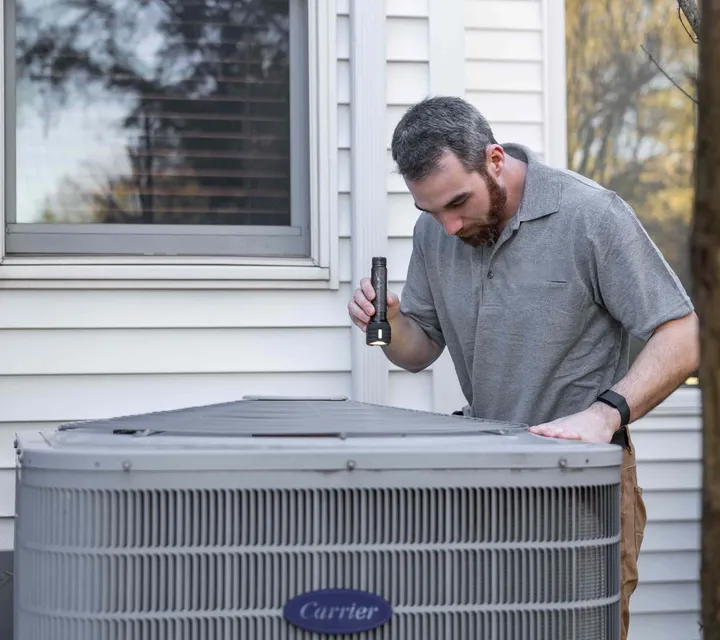 Iron Ridge technician inspecting an AC condenser with a flashlight during a tune-up