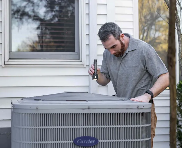 Iron Ridge technician inspecting an AC condenser with a flashlight