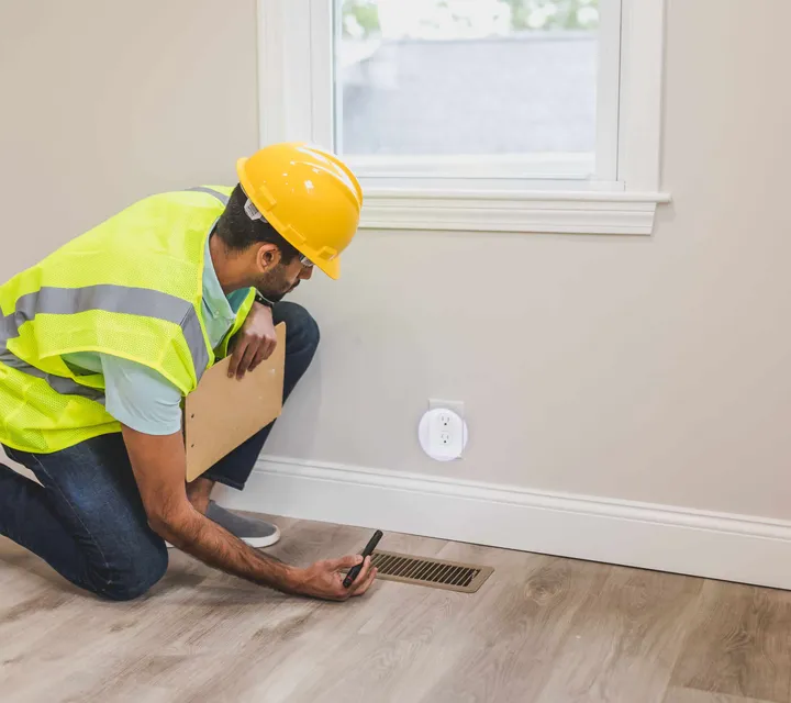Contractor inspecting a supply vent register in a newly built Southern Utah home